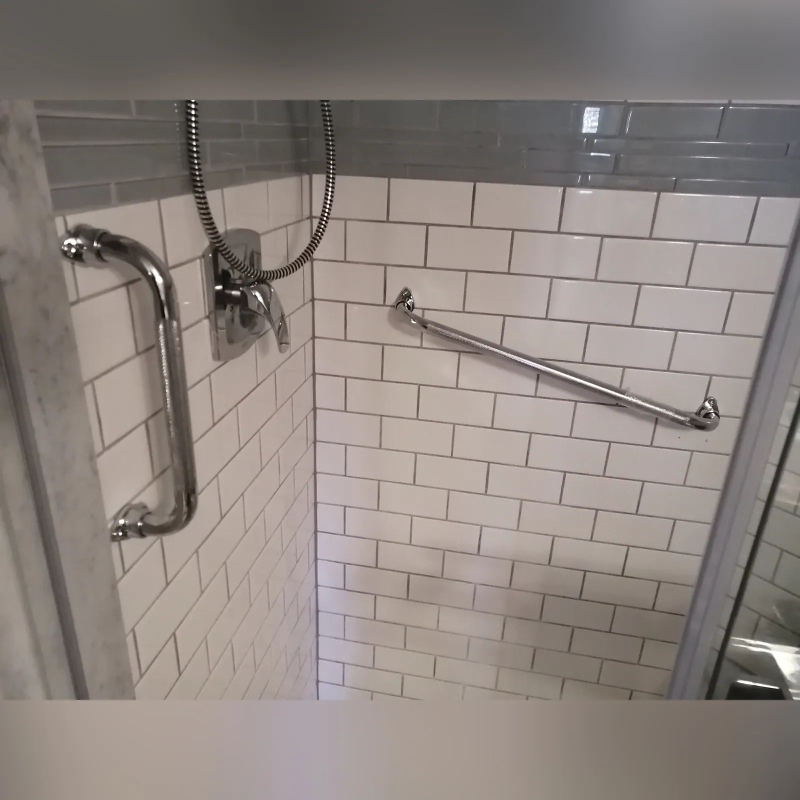 Stainless grab bar fixed into structure in a tiled shower