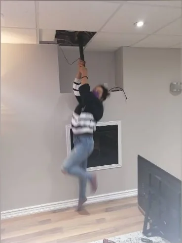 Helperama co-owner hanging from a ceiling-mounted TV bracket to prove it holds
