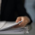 Blurred hand holding a stack of documents on a glass desk with focus on papers.